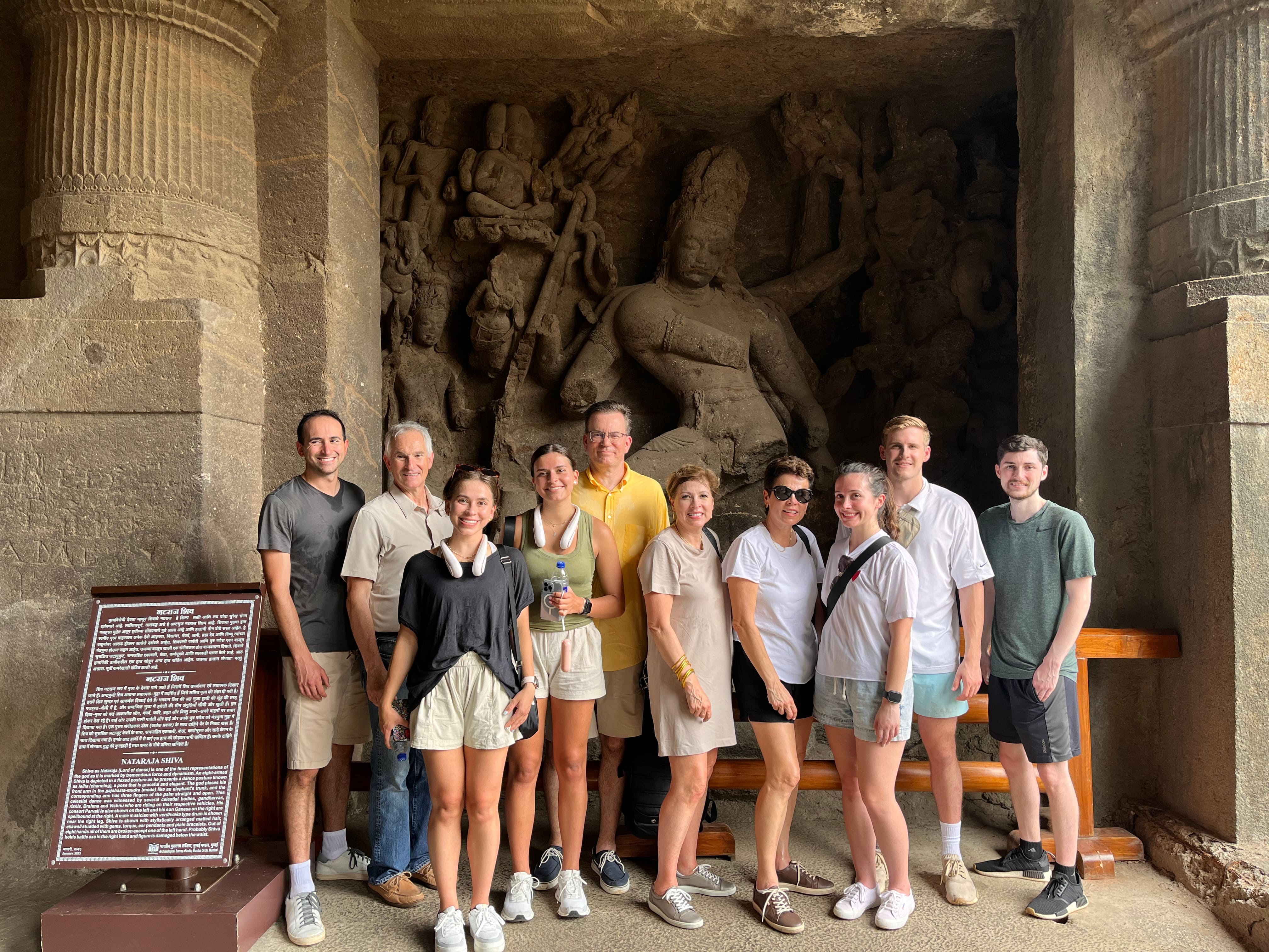 Tour guests posing in front of the iconic Trimurti Shiva sculpture inside Elephanta Caves after a speedboat trip from Mumbai